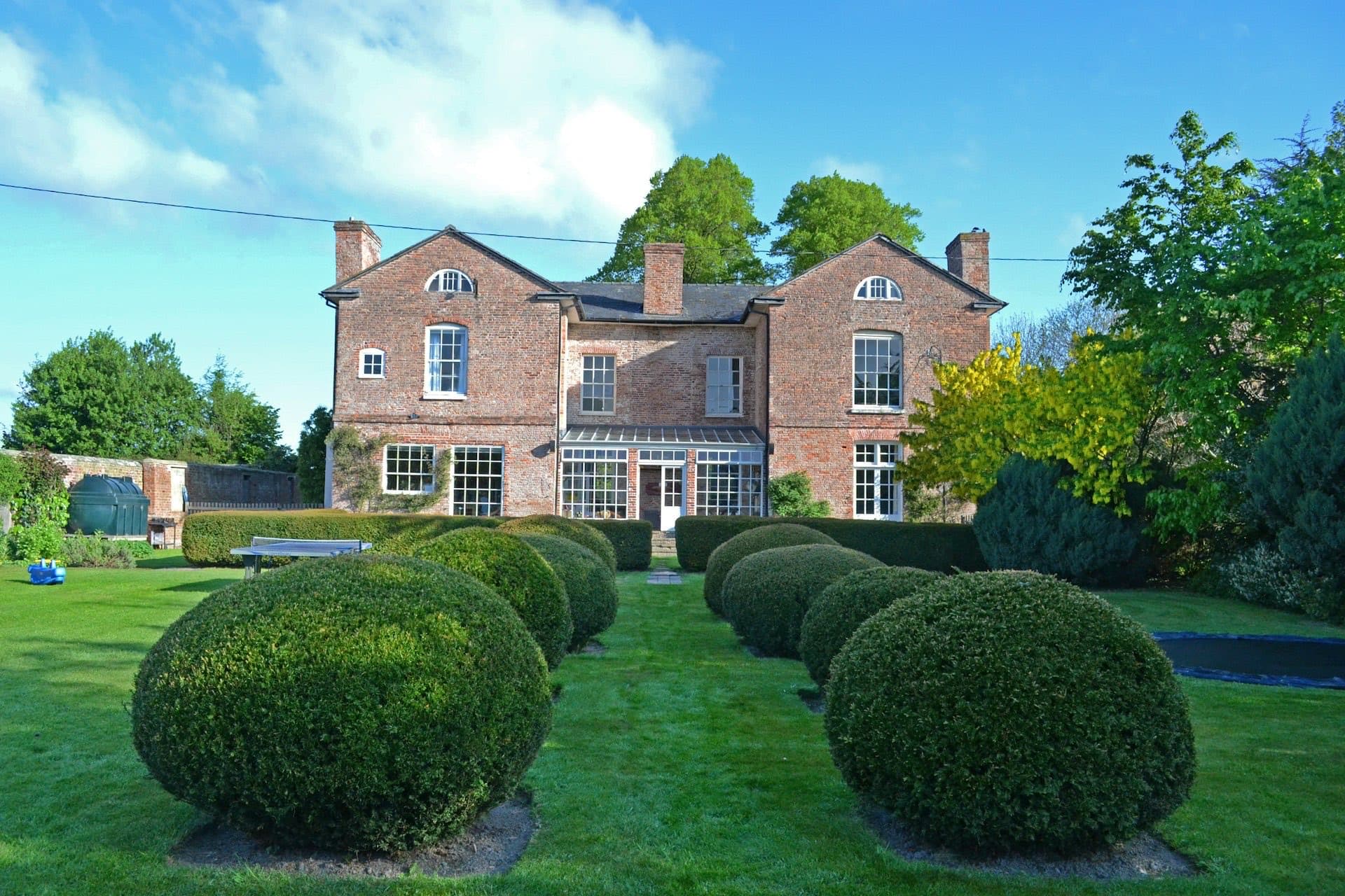 Red-brick period house with a striped, well-kept lawn and topiary